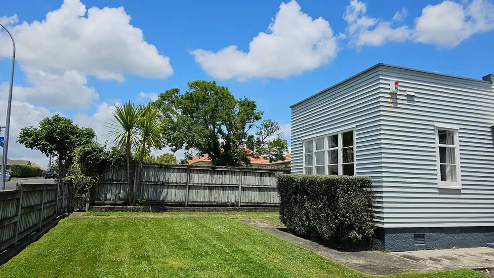 A freshly striped lawn beside a weatherboard house and hedge