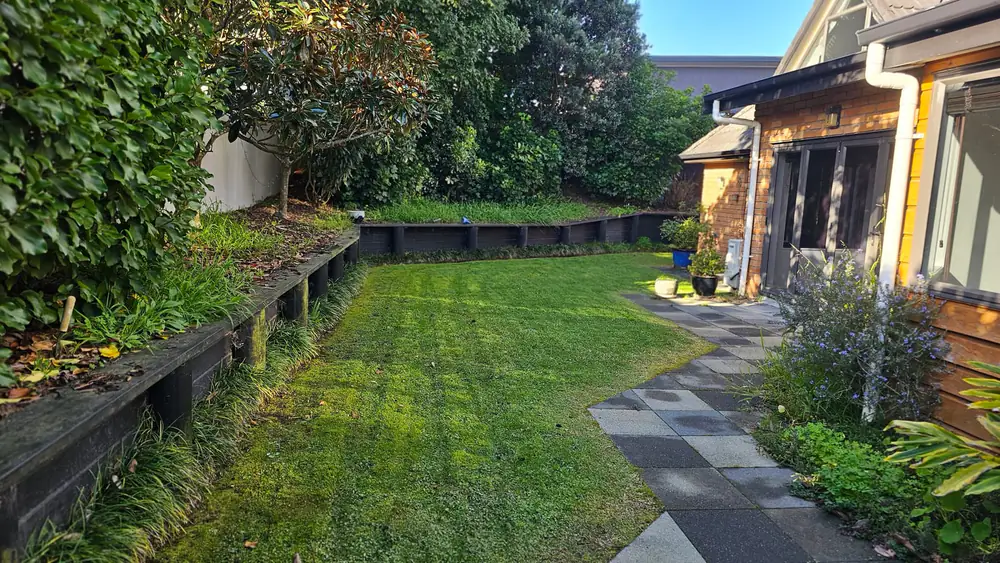 A paved path beside a striped lawn and timber retaining wall